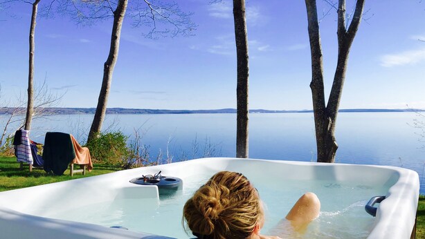 Alguém relaxando em uma banheira de hidromassagem com vista para um lago.