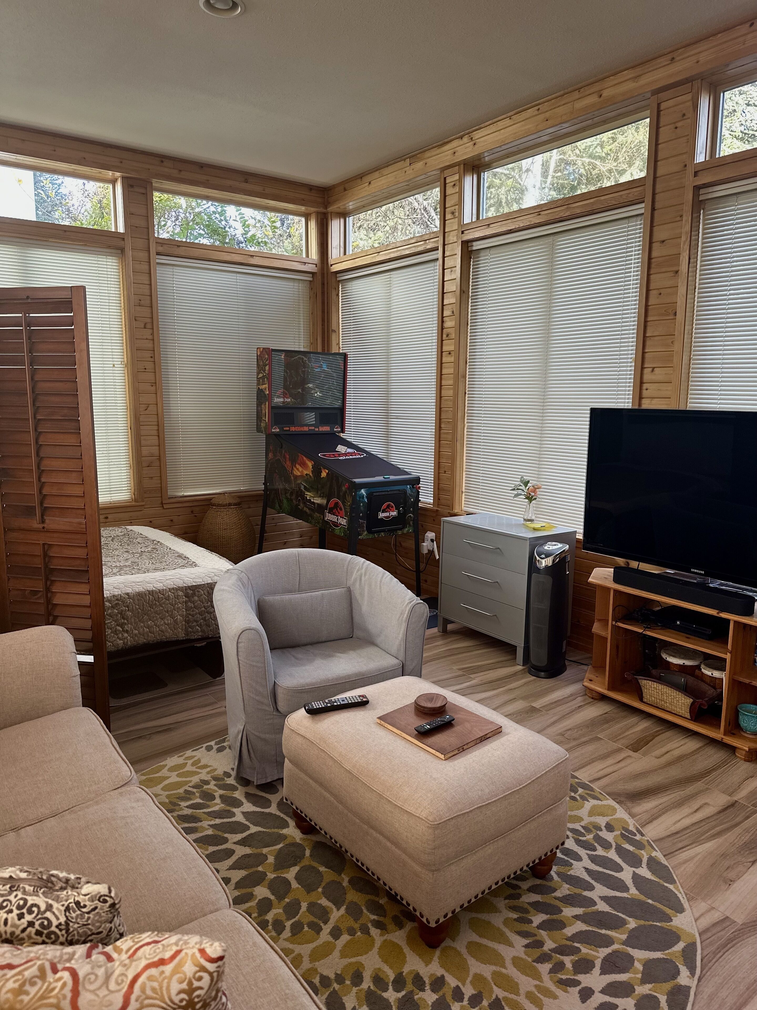 Una sala de estar acogedora con un sofá, un reposapiés y un televisor sobre un mueble de madera.