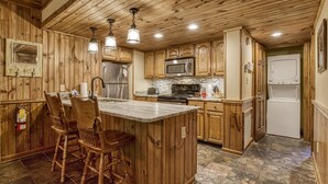 Une cuisine avec des meubles en bois, un îlot central doté de tabourets, des appareils électroménagers en acier inoxydable et un dosseret carrelé.