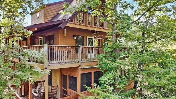 Une cabane en bois à deux étages, dotée d’un balcon à chaque niveau, et entourée d’une végétation luxuriante.