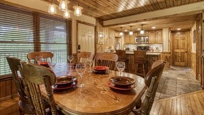 Un coin repas en bois avec une grande table ronde, des chaises et des lampes suspendues.
