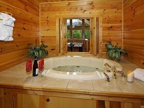 A wooden cabin bathroom with a central bathtub, two potted plants, a towel rack, and a window leading to an outdoor area. - Heavenly Dreams: Beautiful Mountain View - Brand New Hot Tub - Pet Friendly (Sevierville)