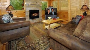 Ein gemütliches Blockhaus-Interieur mit Kamin aus Stein, Holzmöbeln und einem Fernseher.