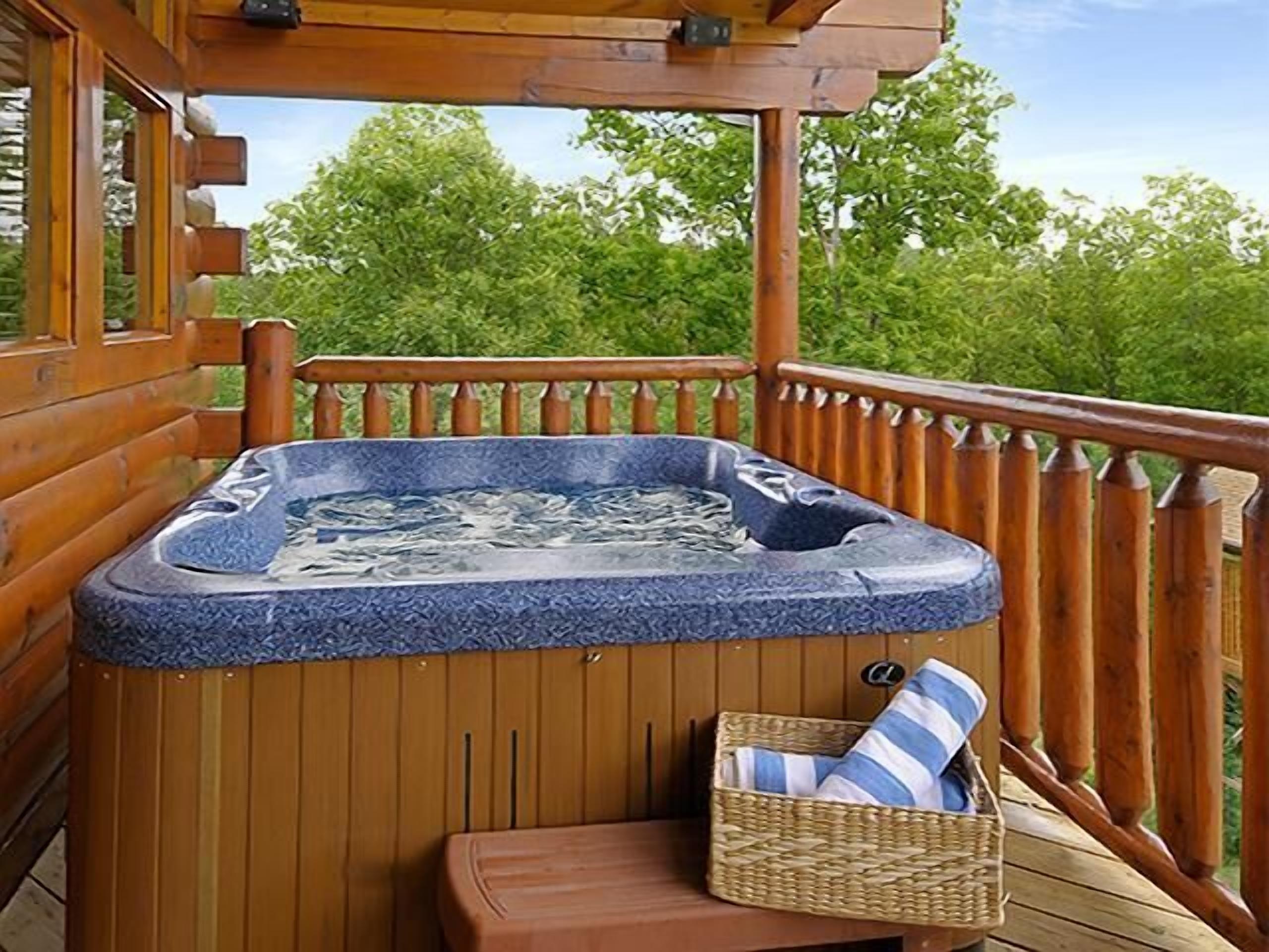 Een houten terras met een jacuzzi, een rieten mand met een gestreept kussen, en een houten bank.