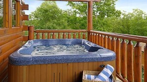 Eine Holzterrasse mit Whirlpool, einem Korbwannenstuhl mit gestreifter Sitzkissen und einer Holzbank.
