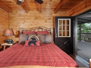 Une chambre à coucher dans une cabane en bois, avec un lit, une table de chevet, une lampe et une porte donnant sur un balcon.