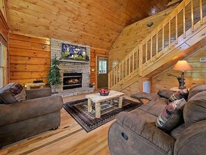 L’intérieur d’un chalet confortable, avec une cheminée, un escalier et un salon meublé de canapés et d’une table basse.