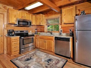 Une cuisine dotée de meubles en bois, d’appareils électroménagers en acier inoxydable et d’un tapis à motifs de pierre.