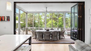 A modern dining area with a table and chairs, large windows, and a view of trees. - Blissful days, barefoot nights at Beach Bliss / Private Pool / Gulf Front Beach Club / 6 Bikes (Santa Rosa Beach)