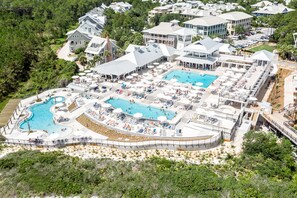 Luftaufnahme eines Resorts mit mehreren Schwimmbecken, Liegestühlen und einer angelegten Grünfläche mit Bäumen.
