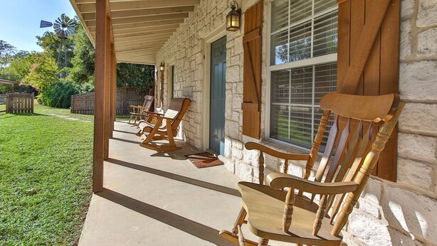 A covered porch with wooden rocking chairs and a stone wall. - Abby's Place 4 - Rocking On Route 66 (Fredericksburg)