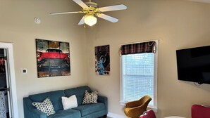 A living room with a blue sofa, a brown chair, a television, and artwork on the walls. - Abby's Place 4 - Rocking On Route 66 (Fredericksburg)