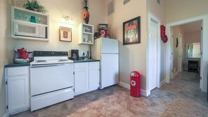 A kitchen with white appliances, a microwave, a stove, and a refrigerator. There is a trash can and a framed picture on the wall. - Abby's Place 4 - Rocking On Route 66 (Fredericksburg)