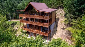 Eine zweistöckige Blockhütte mit einem Balkon im oberen Geschoss, umgeben von dichtem Wald.
