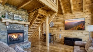 Ein gemütliches Blockhaus-Interieur mit Kamin, einer Holztreppe und einem großen Fernseher an der Wand.