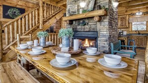 Ein rustikales Holzinnere mit Kamin aus Stein, einer Holztreppe und einem Essbereich, ausgestattet mit weißen Schüsseln und Tellern.