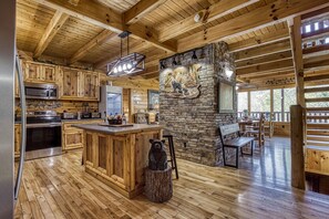 A wooden cabin interior with a kitchen, dining area, and stone fireplace. - Mountain View Gameroom-hot tub-outdoor pool access free wifi pet friendly & more (SEVIERVILLE)