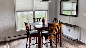 A dining area with a wooden table and chairs, a pendant light, and a large window with blinds. - BEECH MOUNTAIN HIGH - WALK TO SLOPES! (Beech Mountain, NC)