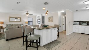 A spacious living area with a large sofa, a dining table with chairs, a kitchen with white cabinets, and a ceiling fan. -  Private Beach Access l CONVENIENCE: 2 minute walk to the Beach! (Santa Rosa Beach)