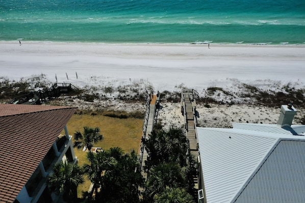 A beach view with a wooden walkway leading to a building with a tiled roof.