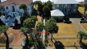 A beachfront property with a central pathway leading to a beach, surrounded by palm trees and a large white building with a red roof. -  Private Beach Access l CONVENIENCE: 2 minute walk to the Beach! (Santa Rosa Beach)