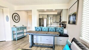 A modern kitchen with a central island, a dining area with a blue sofa, and a living room with a black sofa.