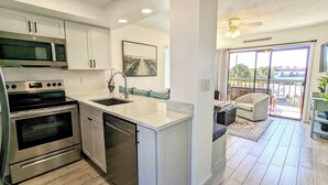A modern kitchen with stainless steel appliances, a large island with a sink, and a dining area with a view of the balcony.