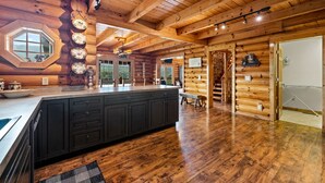 Interior de una cabaña de madera con una isla grande en la cocina, pisos de madera y vistas por una ventana.