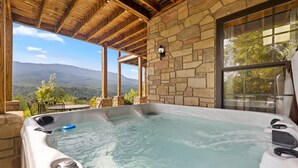 Jacuzzi con vista a montañas, paredes de piedra y techo de madera.
