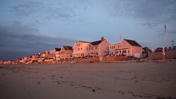 En ejendom ved stranden med flere huse, en sandstrand og en klar himmel.