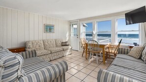 Et værelse med en stribet sofa, en blomstret sofa, et spisebord med stole og et fjernsyn monteret på væggen.