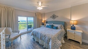 Une chambre à coucher avec un grand lit, une chaise, une table de chevet avec une lampe et une vue sur l’extérieur.