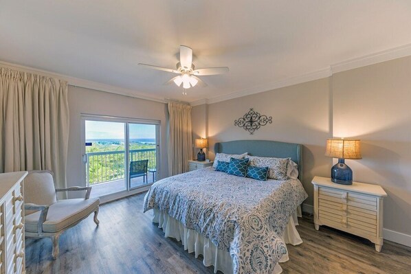 A bedroom with a large bed, a chair, a nightstand with a lamp, and a view of the outdoors. - Large Heated Pool and Hot Tub! Private Beach! (Miramar Beach)