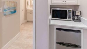 Une cuisine compacte avec des meubles blancs, un four à micro-ondes et un réfrigérateur encastré.