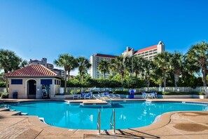 A swimming pool with lounge chairs, a small building with a red roof, and palm trees.