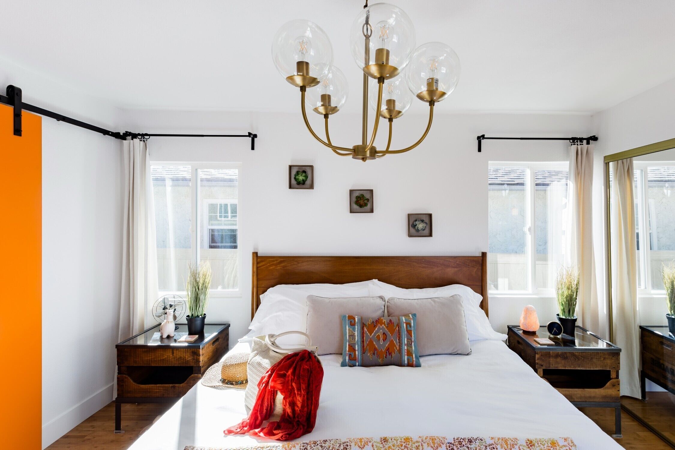 A bedroom with a wooden headboard, a chandelier, bedside tables with lamps, and a window with curtains.
