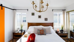Ein Schlafzimmer mit einem hölzernen Kopfende, einer Kandelaberleuchte, Nachttischen mit Lampen und einem fenster mit Vorhängen.
