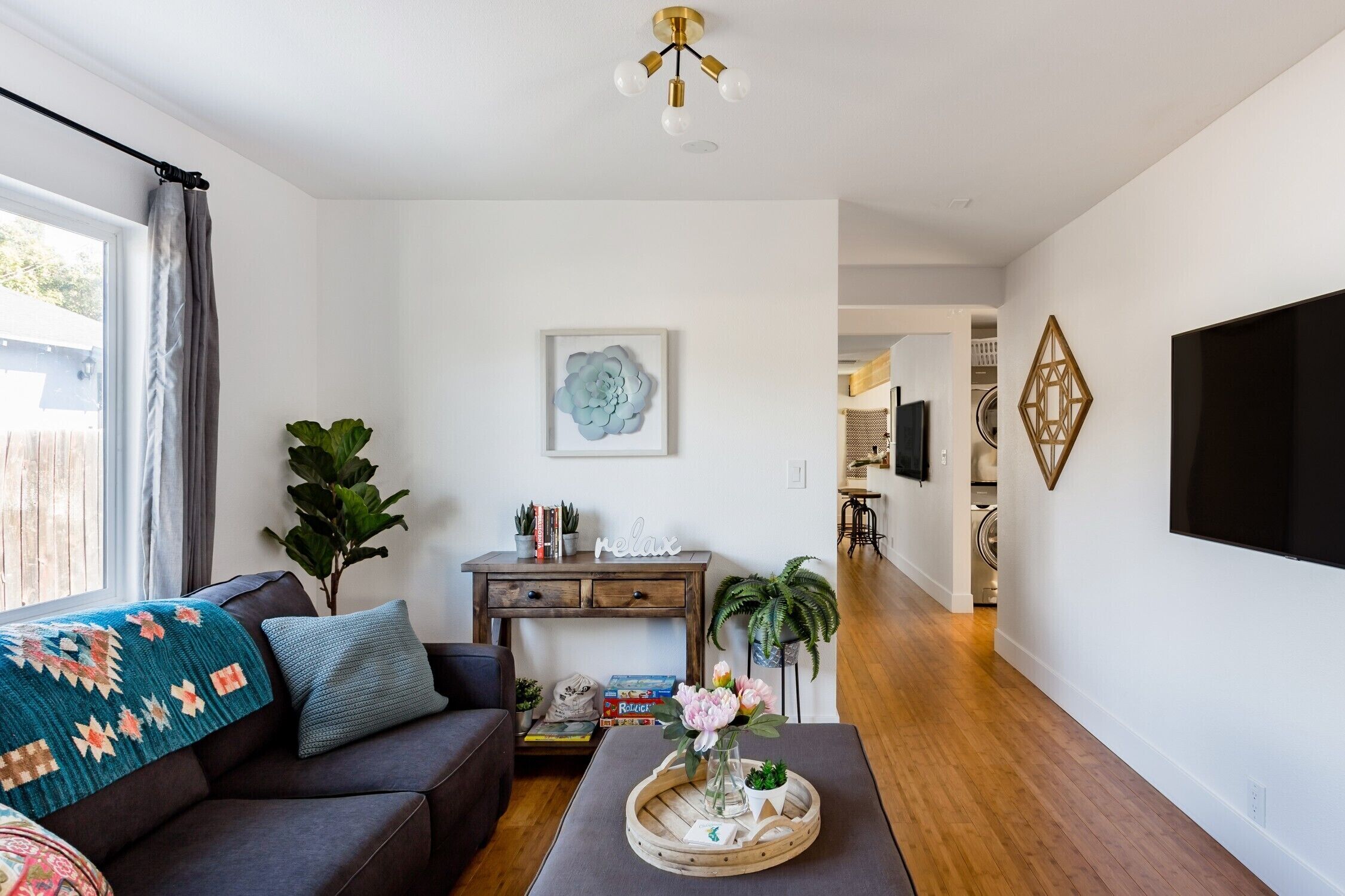 Uma sala de estar com sofá, mesa de centro com bandeja, televisão e parede decorada com motivos geométricos.