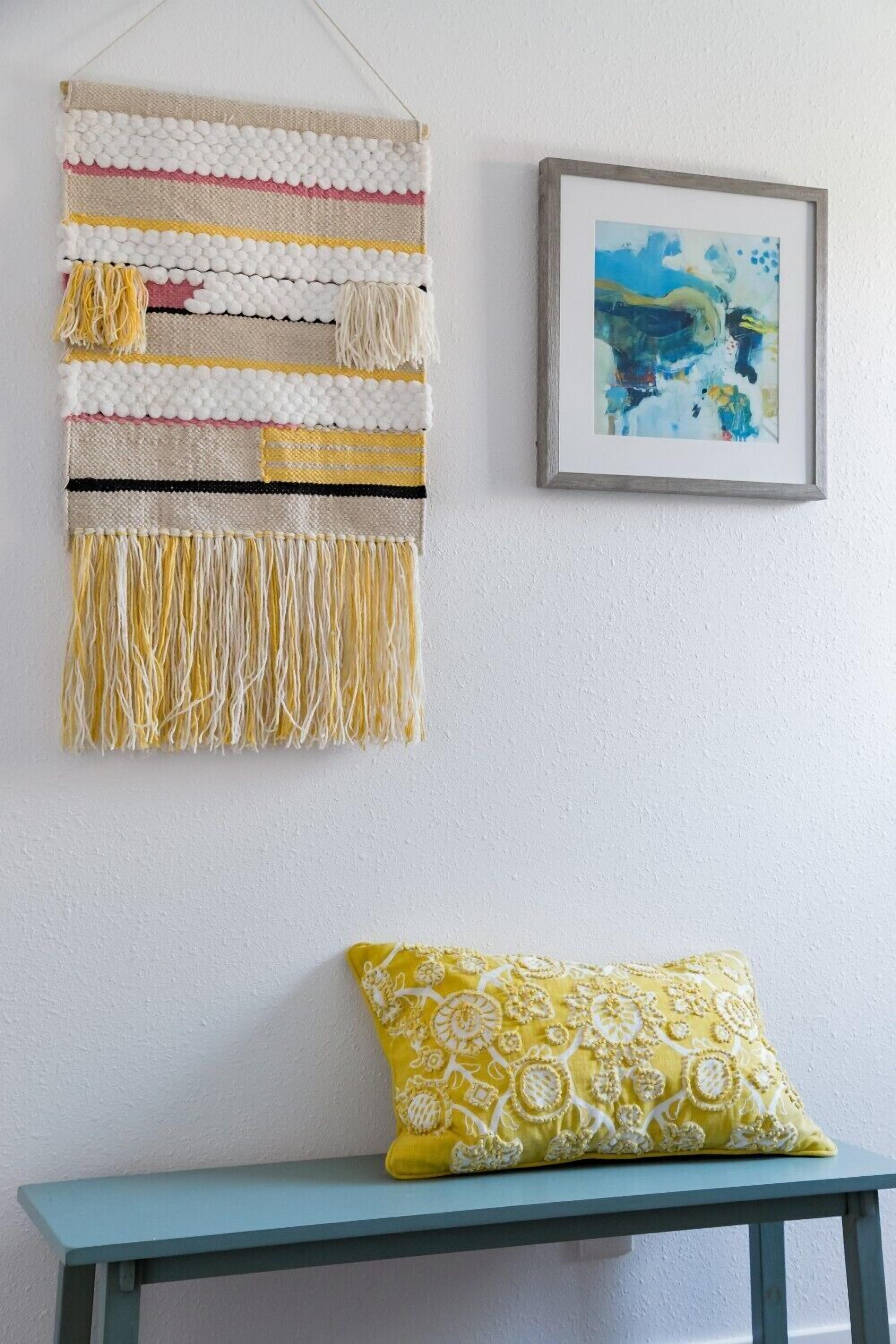 A wall with a decorative woven piece and a framed abstract painting.