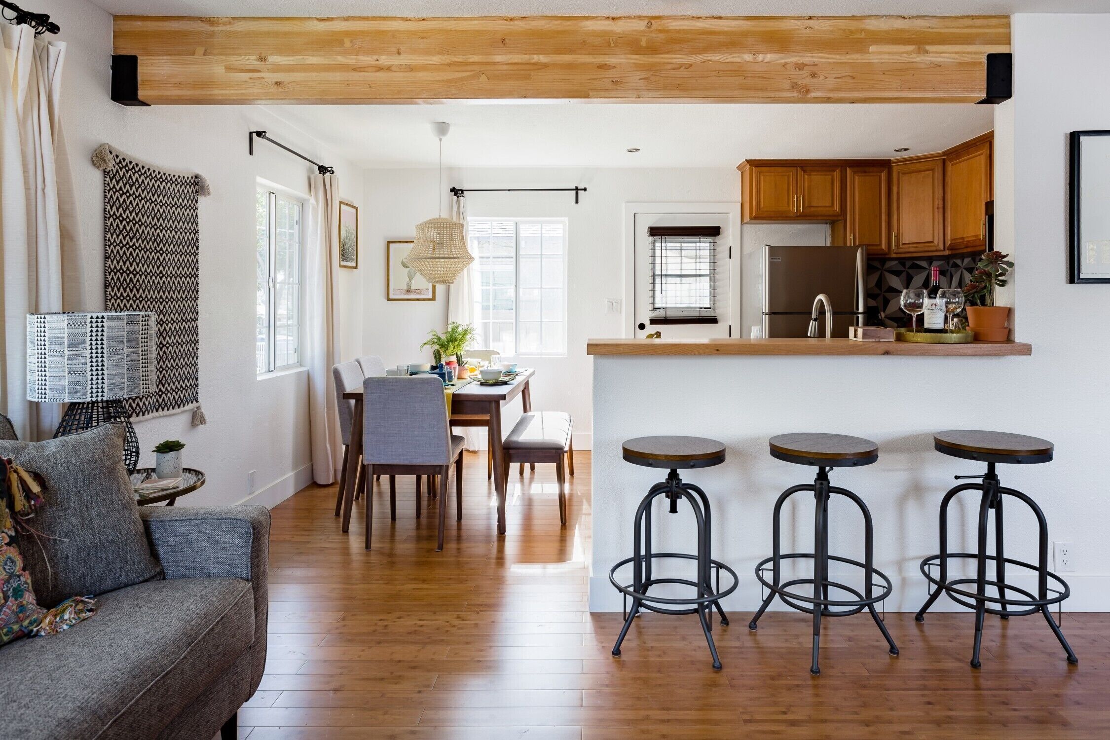A modern kitchen with wooden cabinets, a stainless steel refrigerator, and a bar area with stools.
