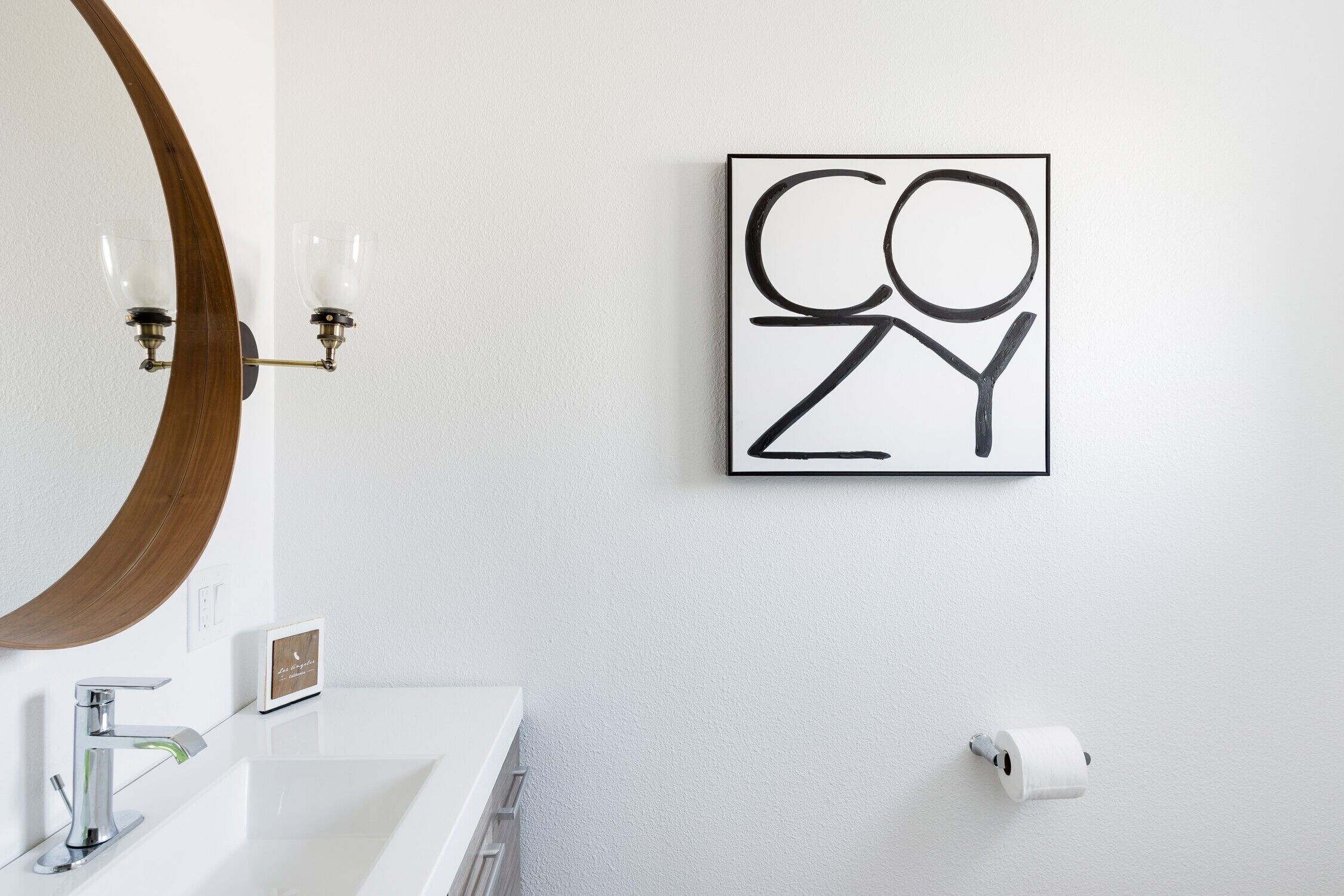 A bathroom with a white sink, a mirror, and a framed artwork on the wall.
