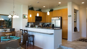 A modern kitchen with wooden cabinets, a stainless steel refrigerator, and pendant lighting. - Excellent for couples or families. Right on the Golf Course. (Waikoloa)