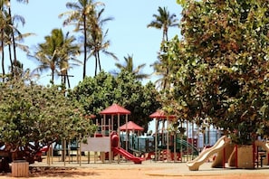 A playground with slides and climbing structures, surrounded by palm trees and a clear sky. - 2B2B Oceanfront Condo, Oceanview in masterbed and living RM ^2026 on sale (Kihei)