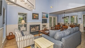 A living room with a fireplace, striped sofa, and a dining area with chairs and a table.