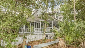 A house with a covered porch, surrounded by trees and a white picket fence.