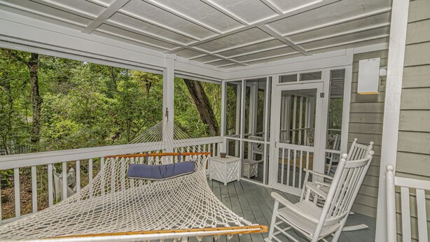 A covered porch with a hammock, rocking chairs, and a view of a forest.