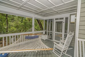 A covered porch with a hammock, rocking chairs, and a view of a forest.