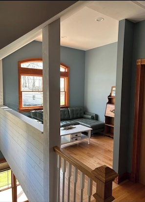 A spacious loft bedroom with a large window, a built-in seating area, and a wooden staircase. - Southold Waterfront with Boat Dock, Boat Ramp, Hot Tub & Beaches (Southold)