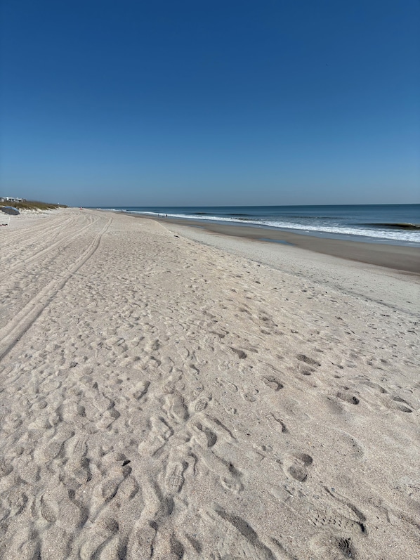En bred sandstrand med fodaftryk og en klar blå himmel.