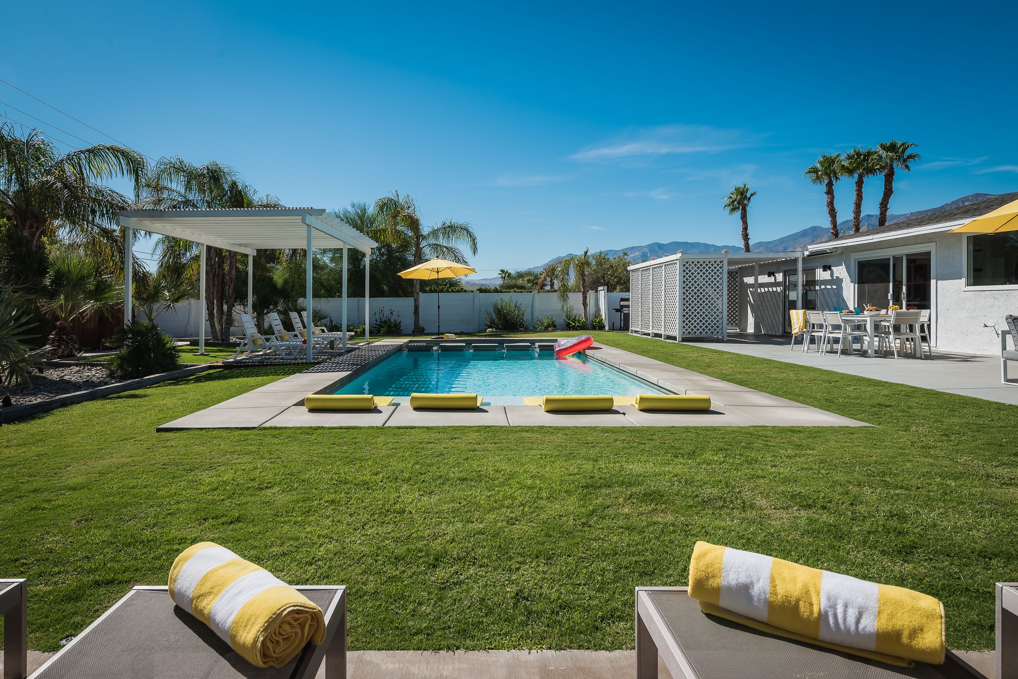 Un jardin avec une piscine, des chaises longues et un espace patio couvert.